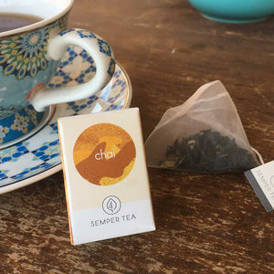 Mini caja de Semper Tea Chai junto a una taza de té y una bolsa piramidal.